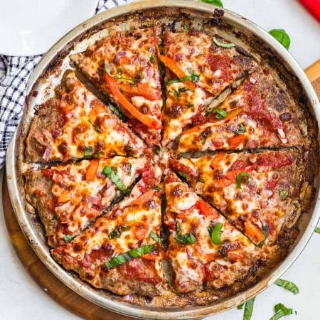Pizza pan with a Meat Crust Pizza on it. White counter with a blue and white napkin in the background.