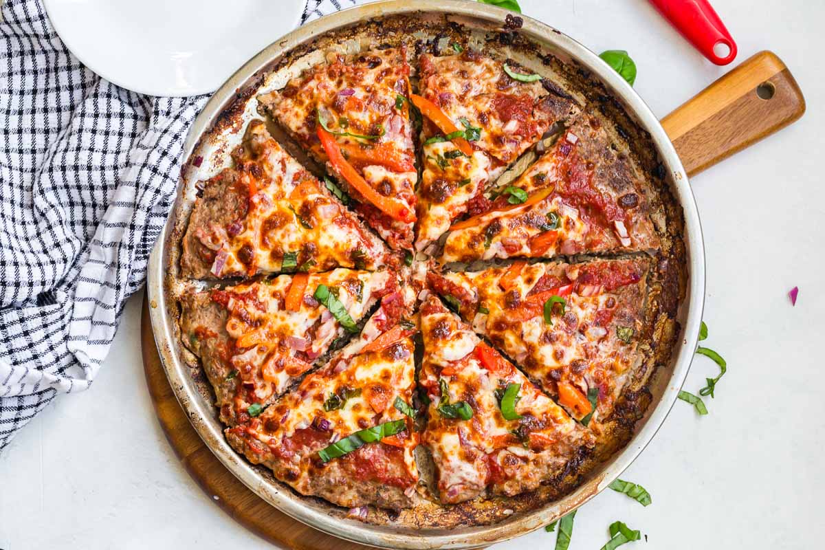 Pizza pan with a Meat Crust Pizza on it. White counter with a blue and white napkin in the background.