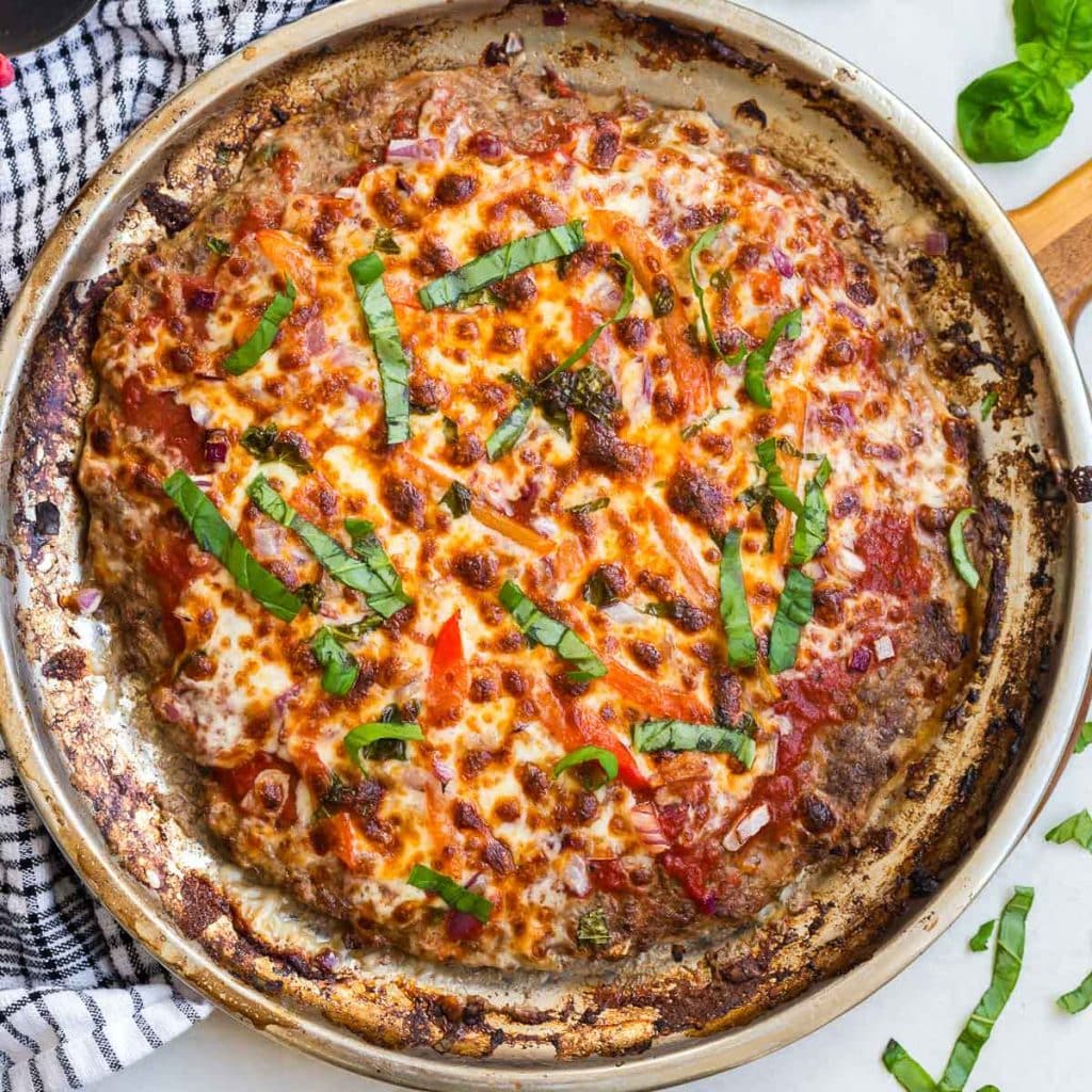 Silver pizza pan with cooked meat base and fresh toppings, just pulled from the oven. 