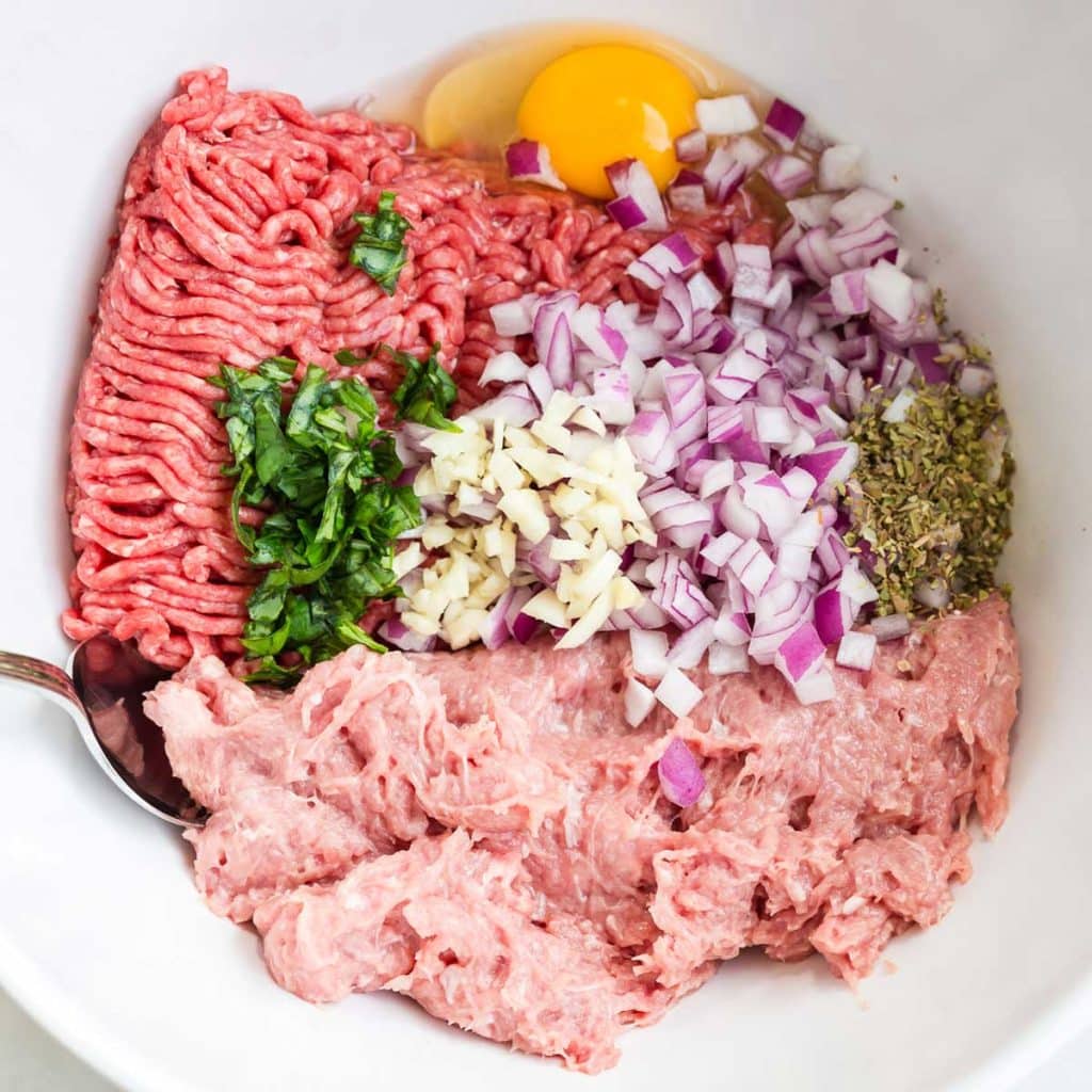 White bowl filled with ground meat, red onions, eggs, and spices.