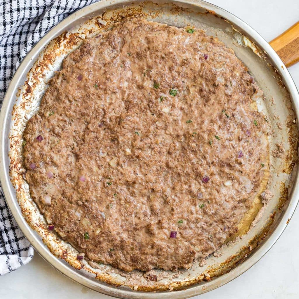 Silver pizza pan with cooked ground meat and spices mixed in.