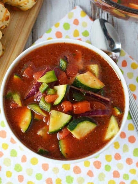White bowl of gazpacho soup in white bowl with breadsticks off to the side.
