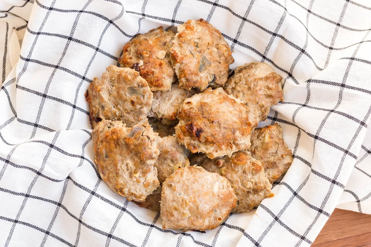 A white and black striped napkin lining a bowl and filled with homemade turkey sausage patties.