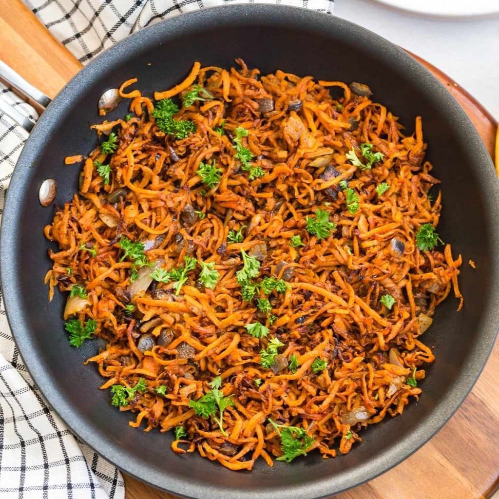 Shredded sweet potatoes in a black skillet being cooked to make sweet potato hash browns.