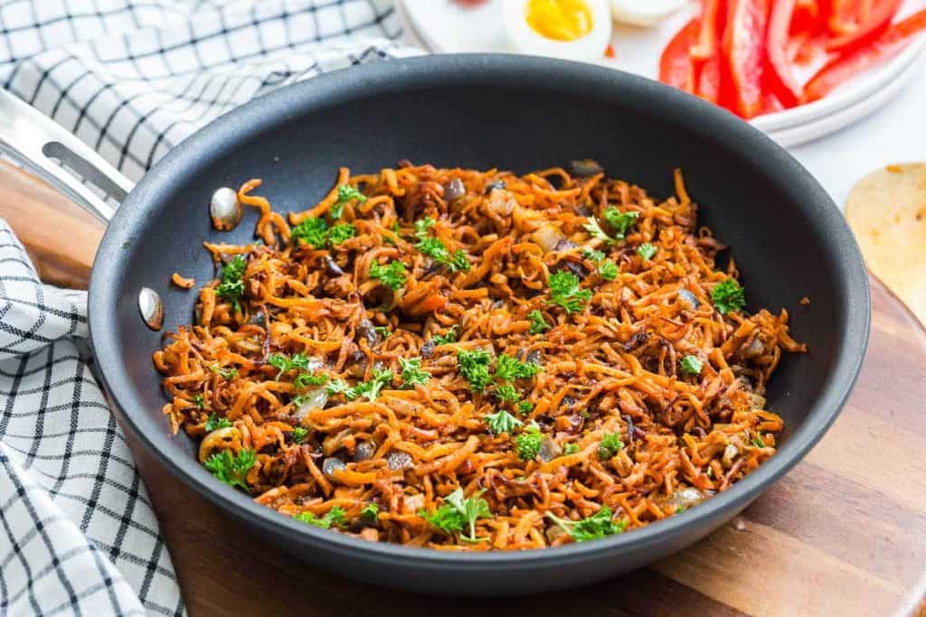 cooked sweet potato hash for weight watchers diet. Cast iron pan is on top of a wood triver with a blue and white dishtowel in the background.