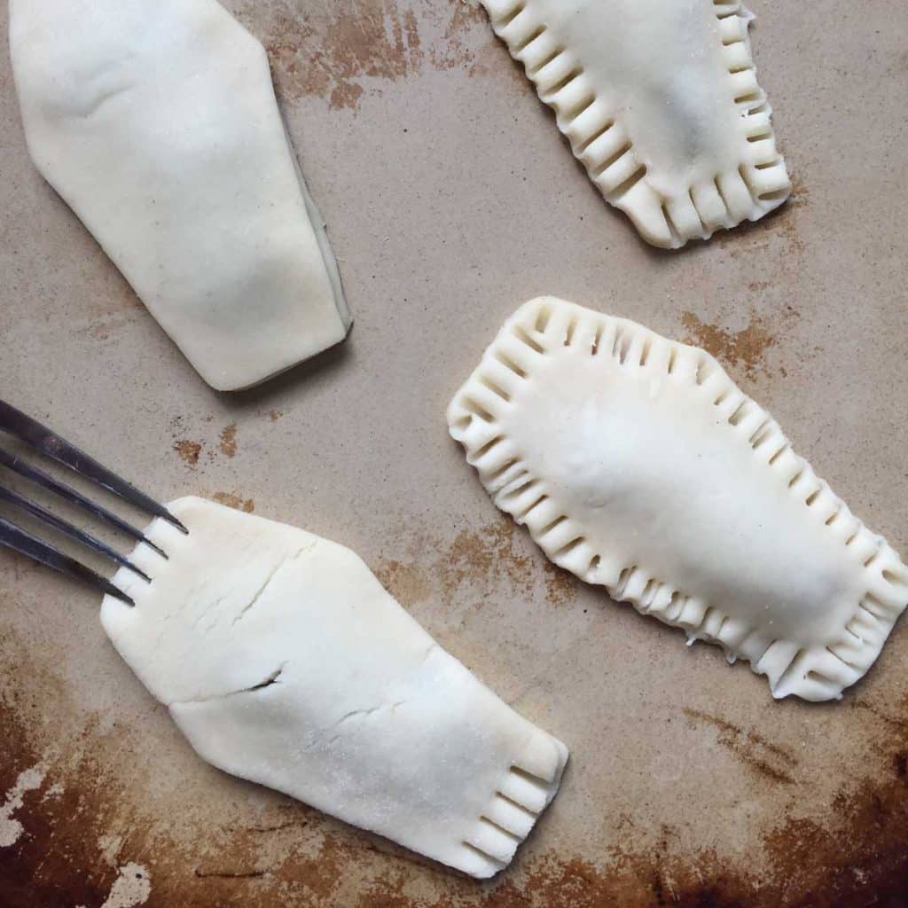 A cooking stone with four coffin shaped pieces of dough that will be made into pop tarts. A fork is shown pressing tines into the outsides of the pop tarts. 