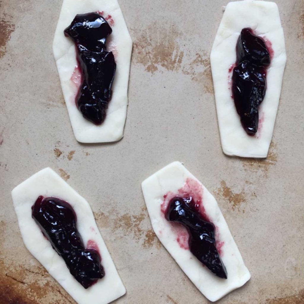 A cooking stone with four coffin shaped pieces of dough with grape jelly inside. 