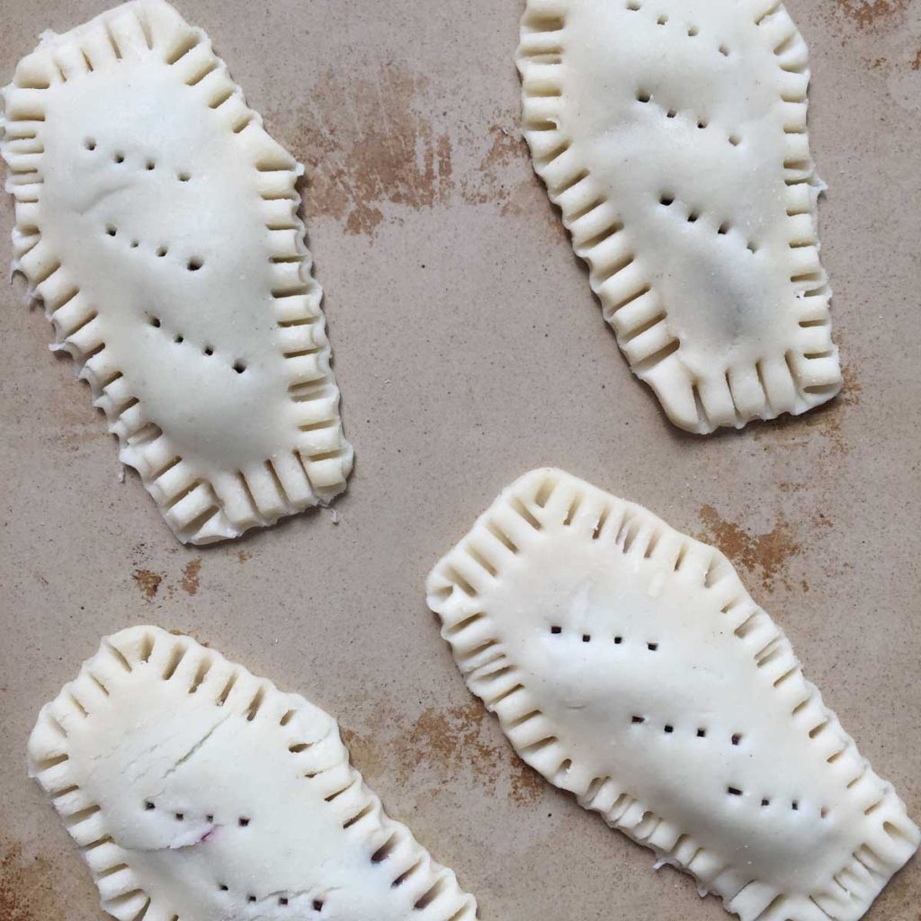 A cooking stone with four coffin shaped pieces of dough that will be made into pop tarts. There are holes poked in them. 