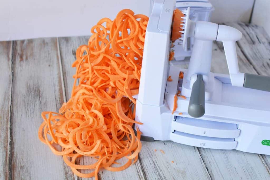 sweet potato being cut into pasta using spiralizer 