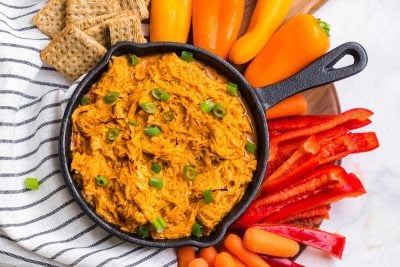 Buffalo Chicken Dip in a cast iron skillet. Around the skillet are crackers, bell peppers, and sliced red bell pepper.