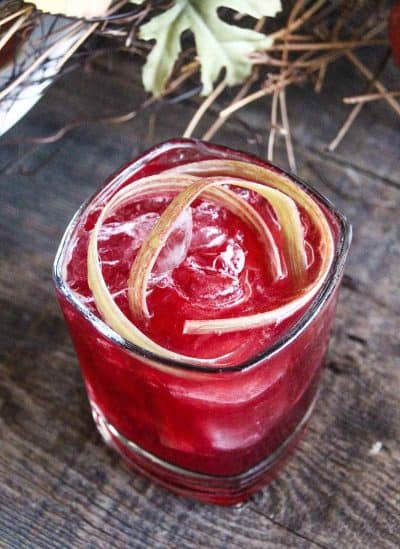 Image of Bourbon Cocktail that is reddish pink in color and garnished with ice and rhubarb parts.