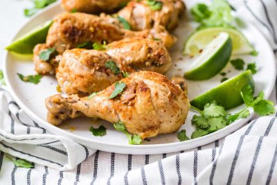 Image of cilantro lime drumsticks on a white plate garnished with cilantro and lime wedges.