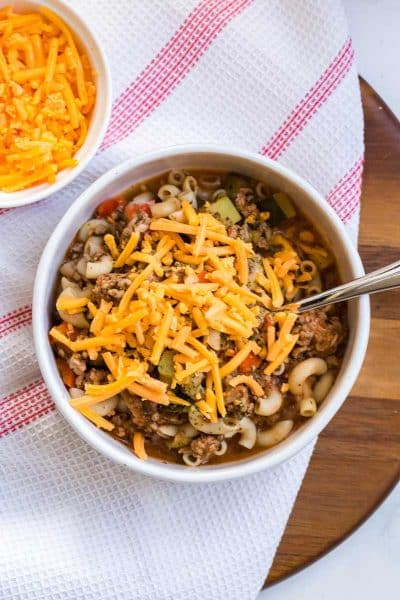 goulash garnished with orange shredded cheese in a white bowl.