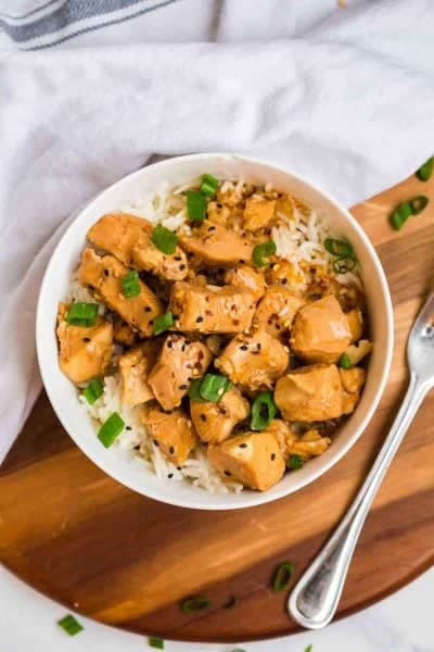 orange chicken recipe in a white bowl. The bowl is on a wooden platter with a fork.