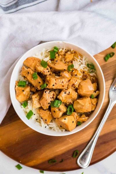 white bowl filled with rice and orange chicken. The bowl is garnished with sliced green onions and sesame seeds.