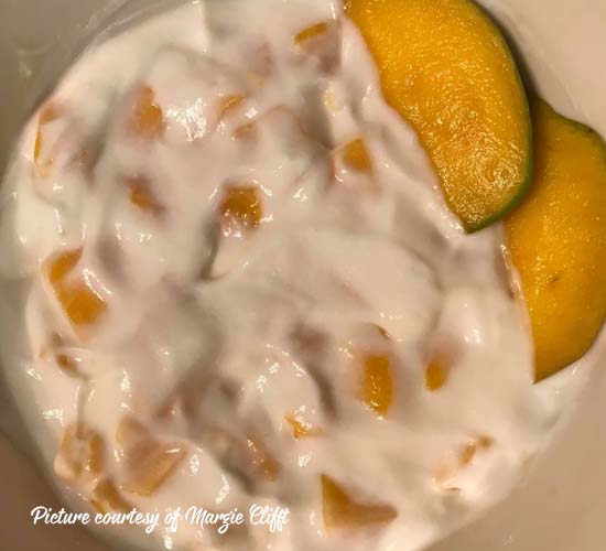 bowl of greek yogurt with chopped mangos mixed in and slices on top