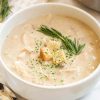 close up of white bowl with soup , croutons, and fresh herbs on top