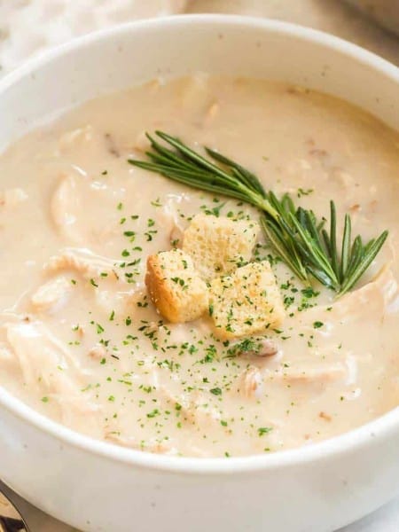 close up of white bowl with soup , croutons, and fresh herbs on top