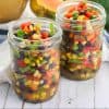 two small mason jars full of summer confetti salad with fresh food in the background