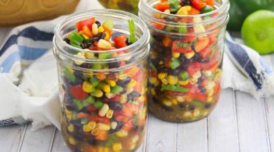 two small mason jars full of summer confetti salad with fresh food in the background