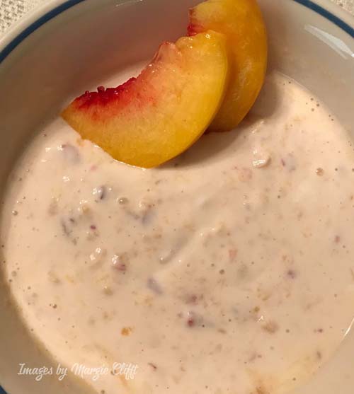 bowl of Greek yogurt with chopped up peaches mixed in, with two peach slices on top