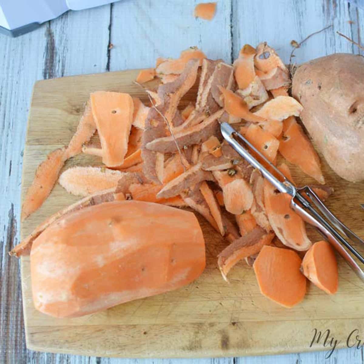 two sweet potatoes on a wooden cutting board being peeled.