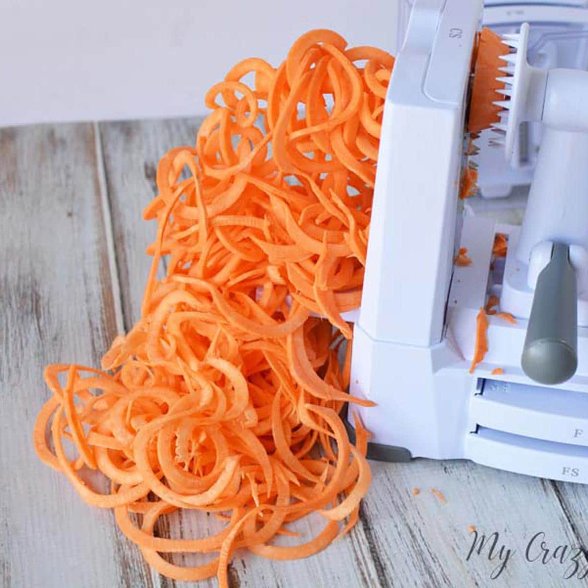 a spiralizer on top of a gray wood counter, spiralizing a sweet potato to make sweet potato pasta.