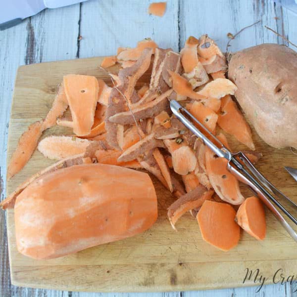 two sweet potatoes on a cutting board being peeled