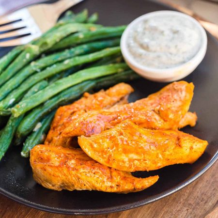 cooked bonelss buffalo wings on a black plate with green beans and ranch