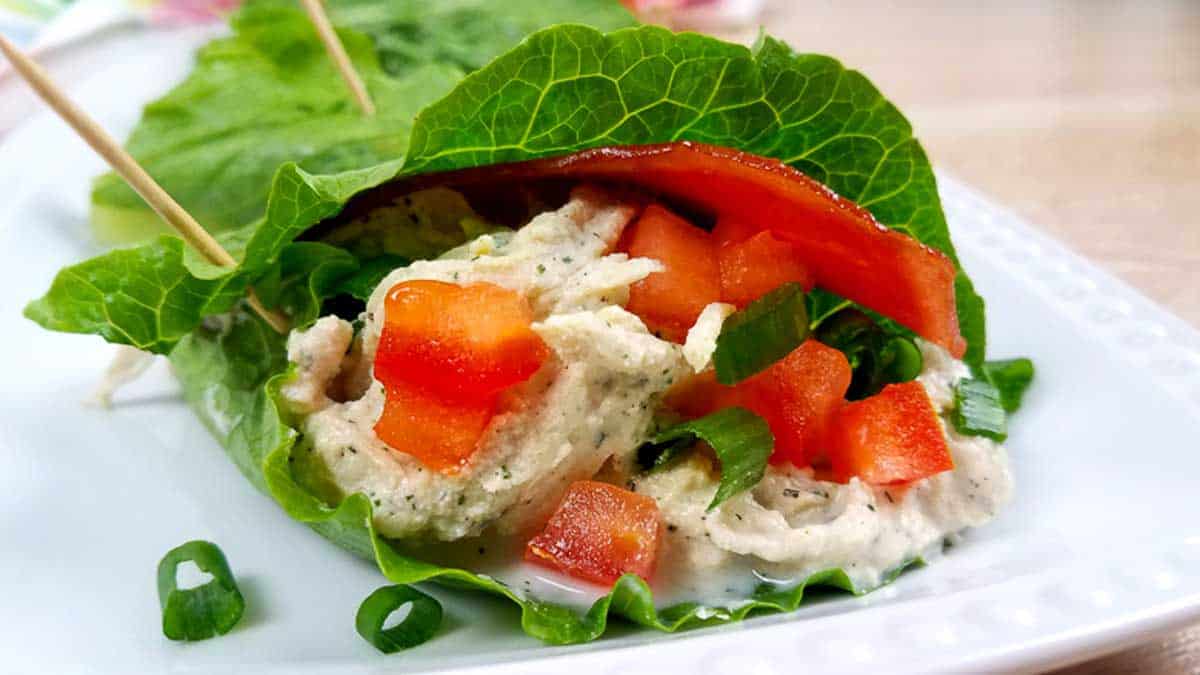 White plate with a lettuce wrap full of crack chicken and diced red peppers and green onions. 
