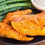 Cooked boneless buffalo wings on a black plate with green beans and ranch.