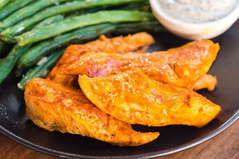 Cooked boneless buffalo wings on a black plate with green beans and ranch.