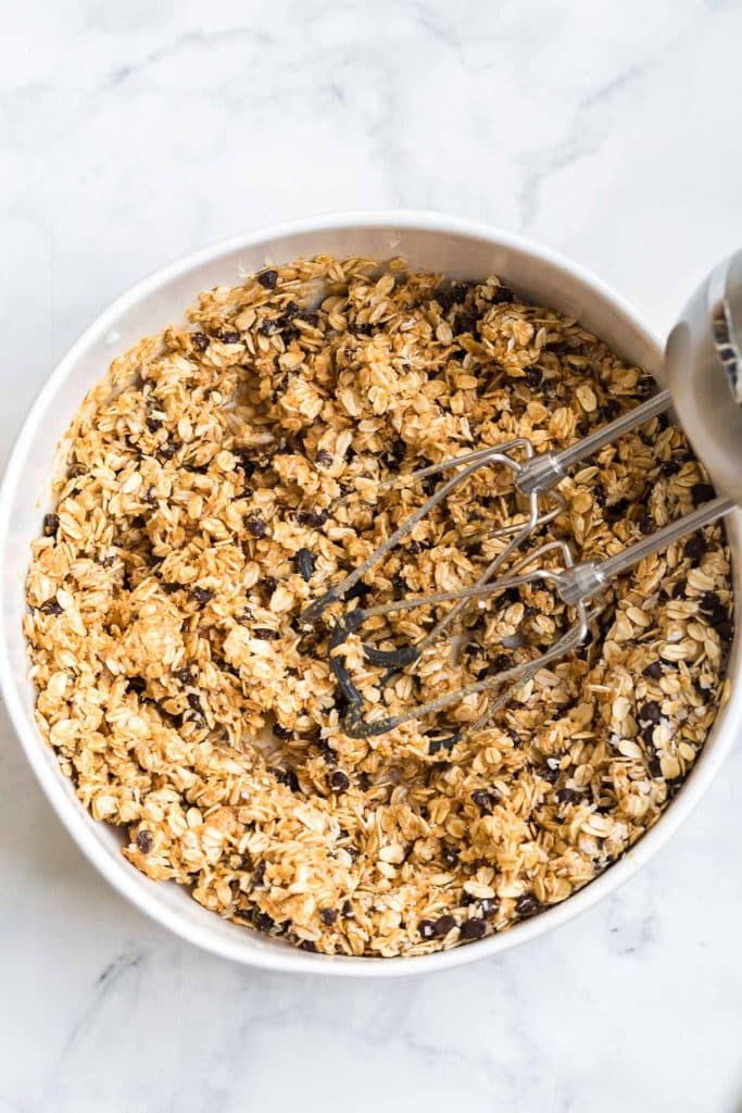 white bowl with oats, chocolate chips, coconut, peanut butter and honey mixed together