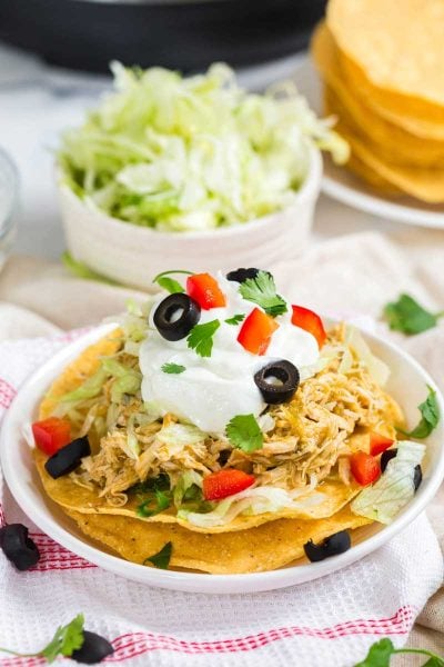 White bowl filled with a tostada garnished with chicken, sour cream, black olives, and tomatoes.