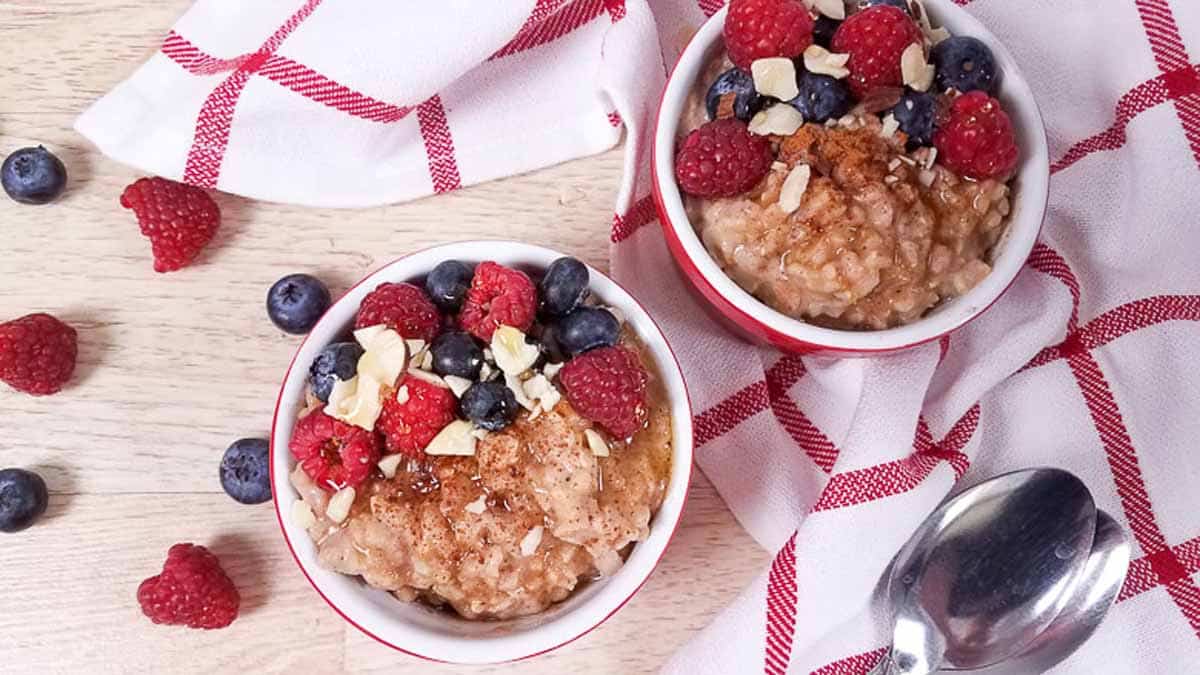 Two red ramekins full of healthy rice pudding. There are berries and slivered almonds on top of the ramekins as well as on the counter to the left of the bowls. 