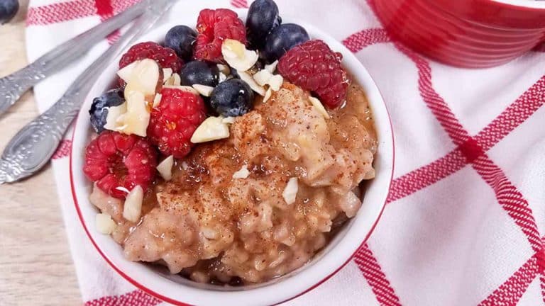 A red ramekin full of healthy rice pudding. There are berries and slivered almonds on top of the ramekin and a white and red striped napkin underneath.