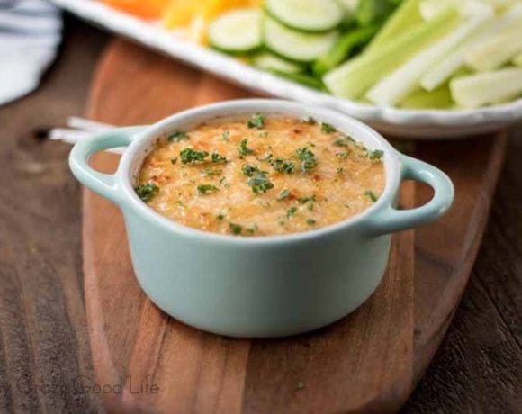 Baked Buffalo Chicken Dip in a white ramekin with two handles in front of a tray of fresh cut mixed veggies.