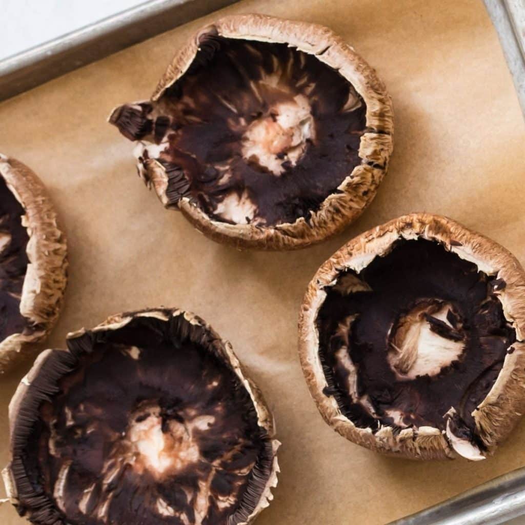 Four cleaned portobello mushrooms on a parchment lined baking sheet.
