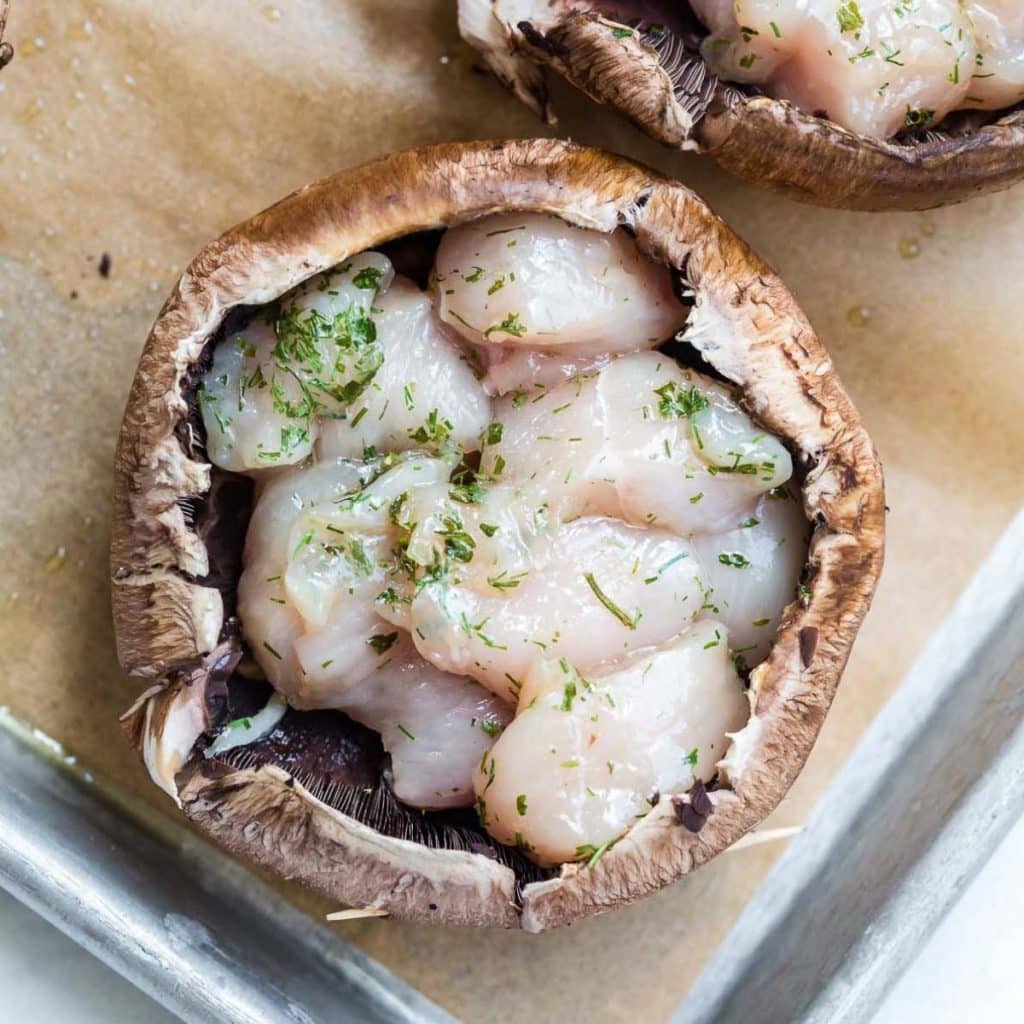 A portobello mushroom stuffed with uncooked diced chicken and seasonings.