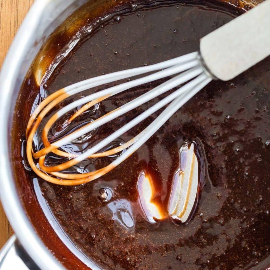 A sauce pan of balsamic vinegar and honey being cooked and stirred with a whisk.