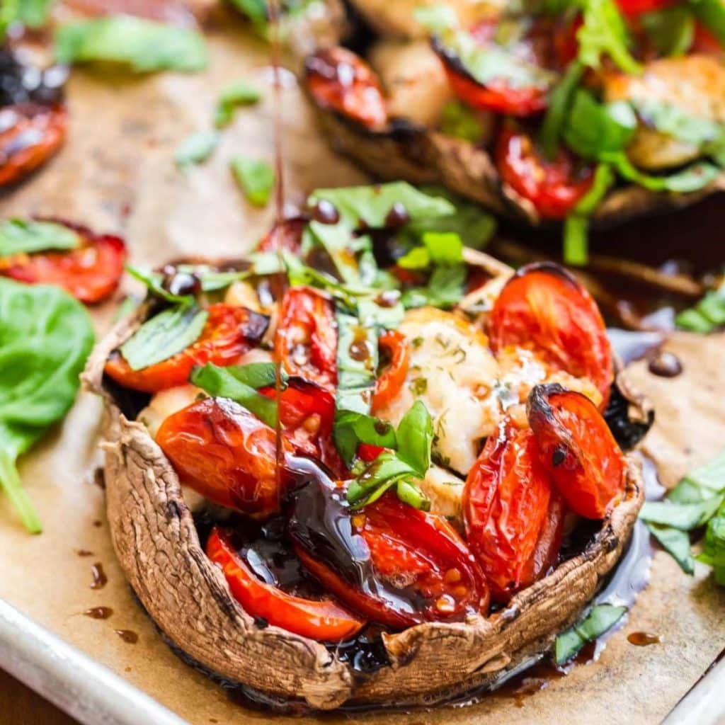 A cooked portobello mushroom stuffed with chicken and tomatoes and topped with fresh basil and a drizzle of balsamic reduction.