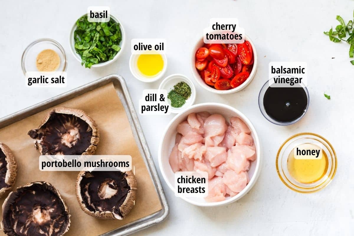 A white counter top with bowls of labeled ingredients needed to make Caprese Chicken Stuffed Portobello Mushrooms.