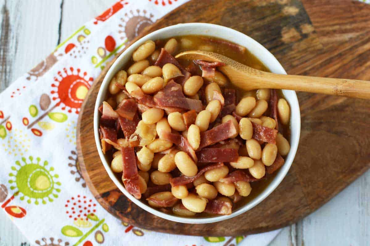 Homemade healthy pork and beans in a white bowl on top of a wooden board.