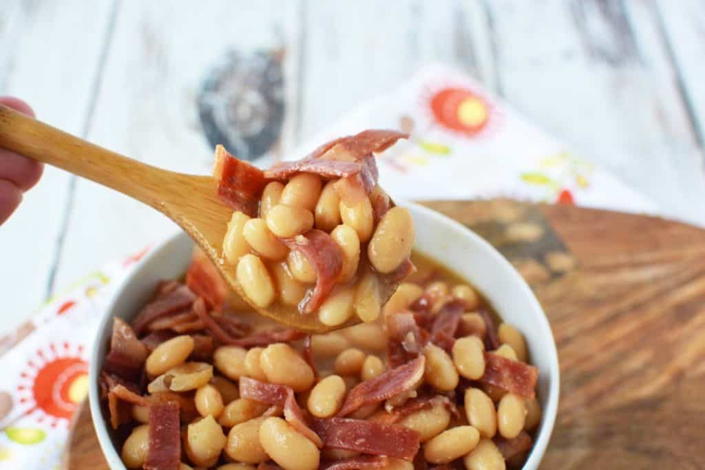 bowl of healthy pork and beans with wooden ladle holding up a spoonful.