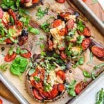 Four portobello mushrooms on a baking sheet that have been cooked with chicken and tomatoes and topped with fresh basil and a balsamic reduction.