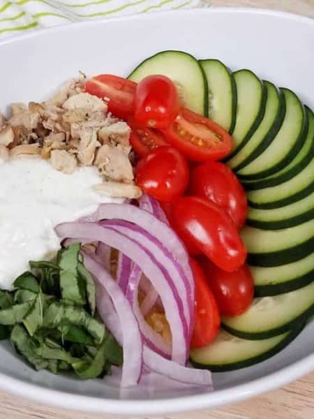 white bowl with cooked chicken gyro bowl, spaghetti squash, and fresh veggies.