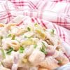 close up of creamy noodles with chicken and chives and a red and white napkin in the background