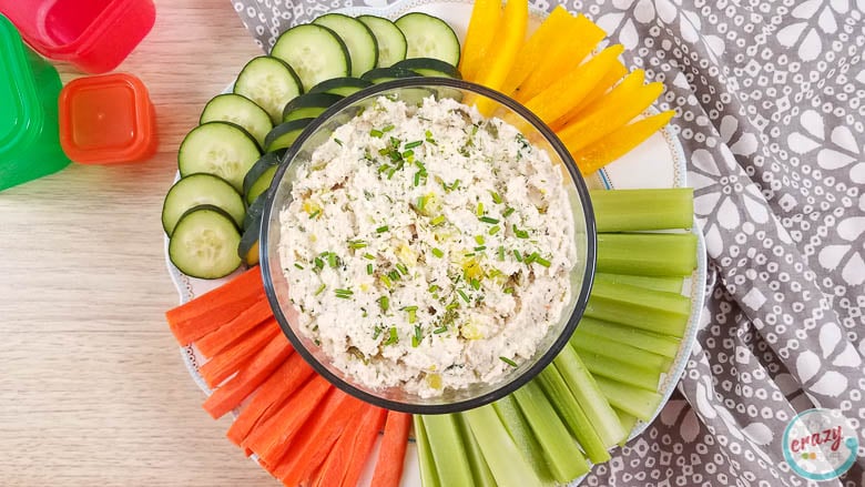 image of dill pickle chicken dip in a clear glass bowl with colorful dipping veggies