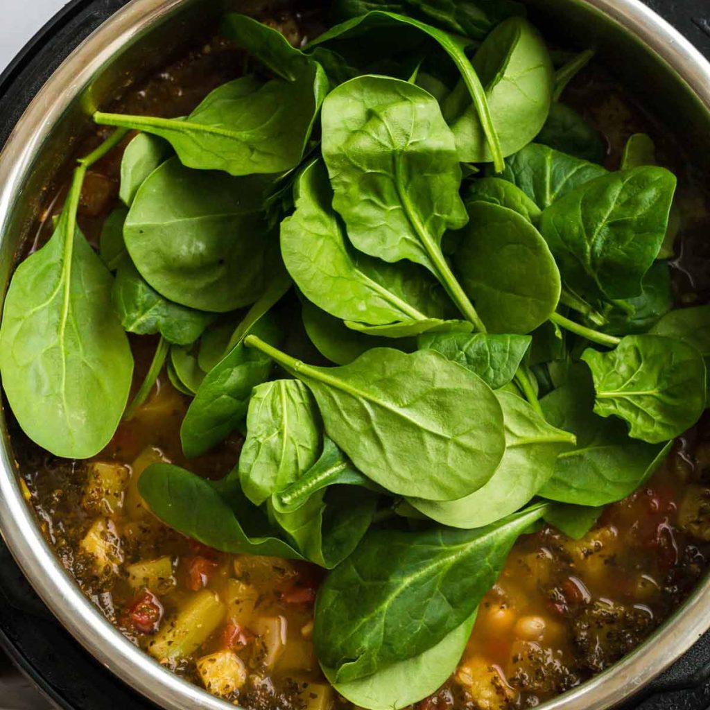 Instant Pot with cooked Minestrone soup and fresh spinach on top.