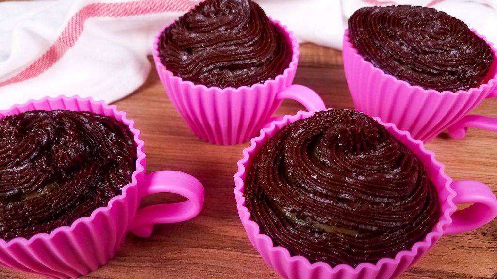 pink silicone tea cups with cupcakes baked inside of them with chocolate frosting.